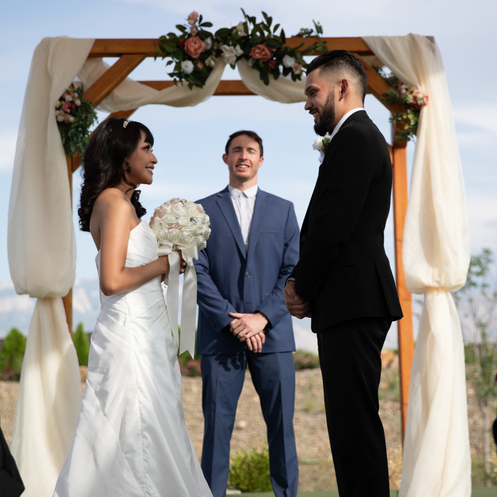 A couple stands under an arch dressed for a wedding